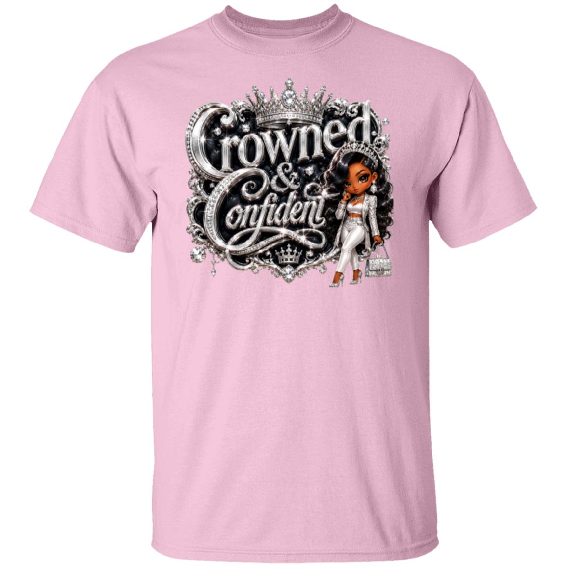 A light pink short-sleeve crewneck t-shirt featuring a large graphic print on the front. The graphic displays the text 'Crowned & Confident' in a stylized silver font with a crown above, alongside an illustration of a woman in a white outfit holding a handbag.