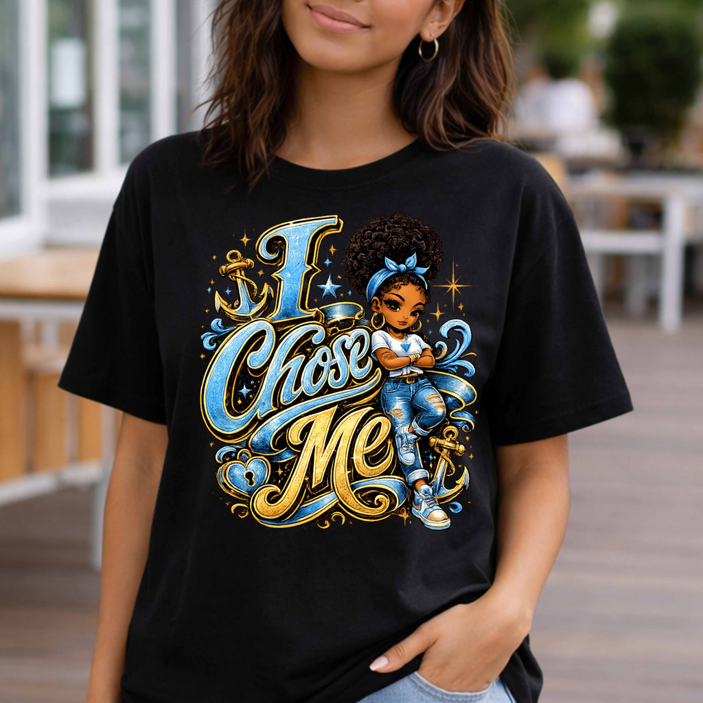 A woman wearing a black graphic t-shirt with a colorful illustration of a girl and the text 'I Chose Me' in blue and gold script, set against a blurred outdoor background.