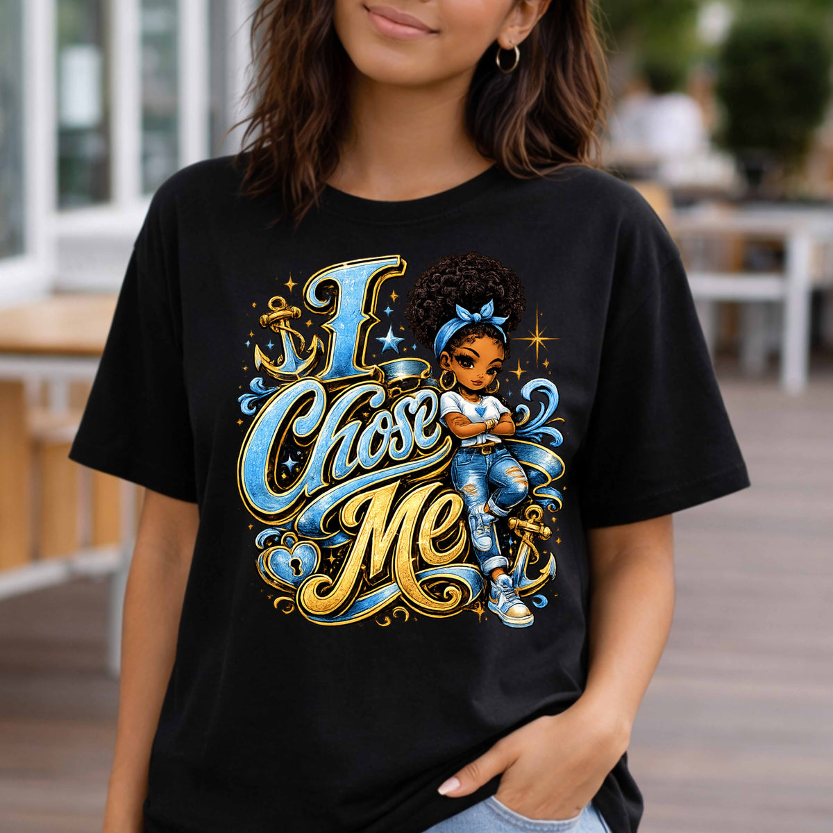 A woman wearing a black graphic t-shirt with a colorful illustration of a girl and the text 'I Chose Me' in blue and gold script, set against a blurred outdoor background.