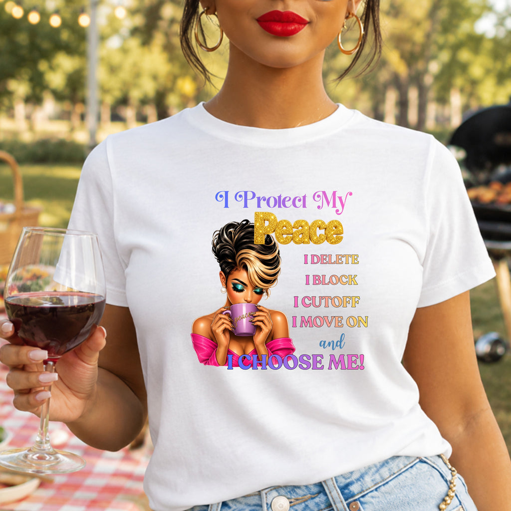 A woman wearing a white graphic t-shirt with a colorful text design that reads 'I Protect My Peace I DELETE I BLOCK I CUTOFF I MOVE ON and I CHOOSE ME!' accompanied by an illustration of a woman holding a mug. She is holding a glass of red wine in an outdoor park setting.